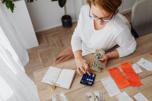 Visão de cima de uma mulher organizando contas, dinheiro e uma calculadora para controlar as despesas domésticas.