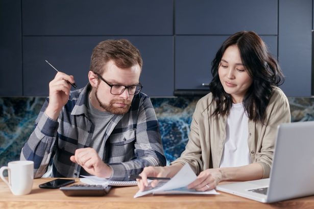 Casal calcula contas e organiza as finanças domésticas sentado à mesa em casa.