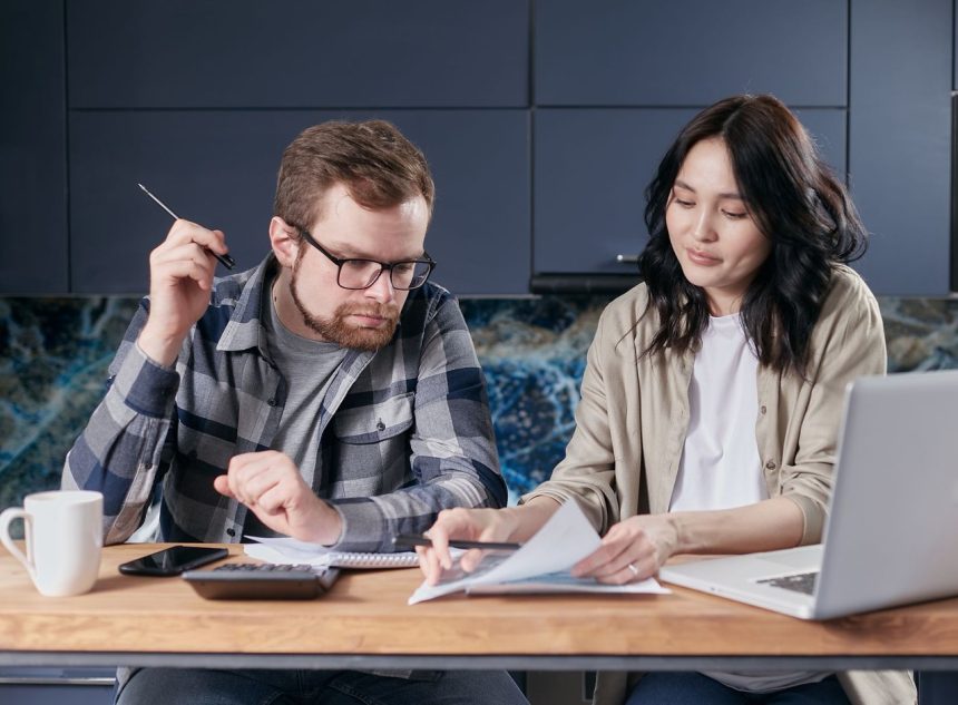 Casal calcula contas e organiza as finanças domésticas sentado à mesa em casa.