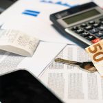 Documentos financeiros ao lado de uma calculadora, smartphone, nota de euro e chave, representando o controle e a gestão de despesas.