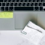 Laptop com lembrete adesivo e recibos sobre uma mesa, representando a organização para a declaração e a consulta do Imposto de Renda