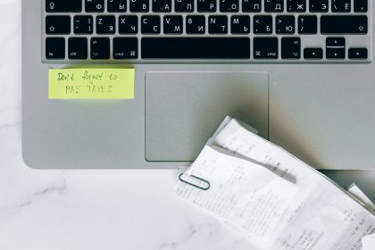 Laptop com lembrete adesivo e recibos sobre uma mesa, representando a organização para a declaração e a consulta do Imposto de Renda