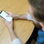 Pessoa segura um smartphone sobre uma mesa de madeira; a tela está em branco.
