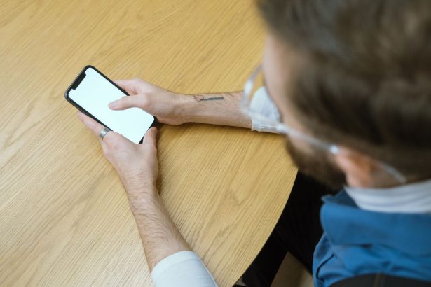 Pessoa segura um smartphone sobre uma mesa de madeira; a tela está em branco.