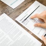 Mão analisa um contrato de cartão de crédito sobre uma mesa de madeira.