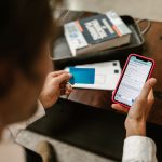 Pessoa realiza um pagamento online pelo celular enquanto segura um cartão bancário.