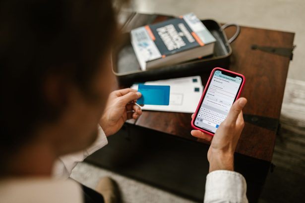Pessoa realiza um pagamento online pelo celular enquanto segura um cartão bancário.